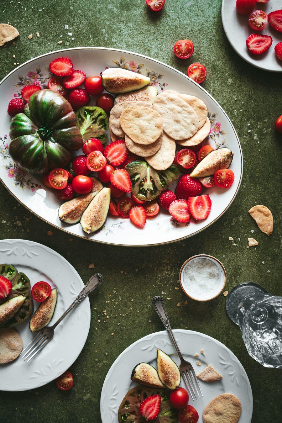 Bandeja con tomates, fresas, higos y galletas sobre fondo verde oliva