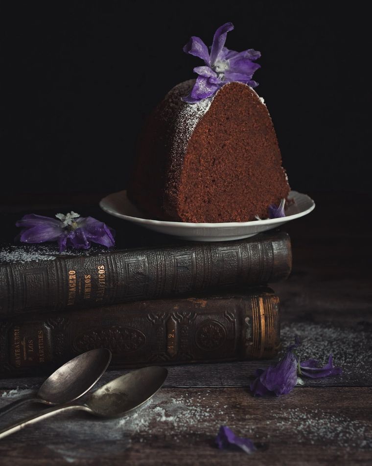 Bizcocho de chocolate con flores violetas sobre libros antiguos
