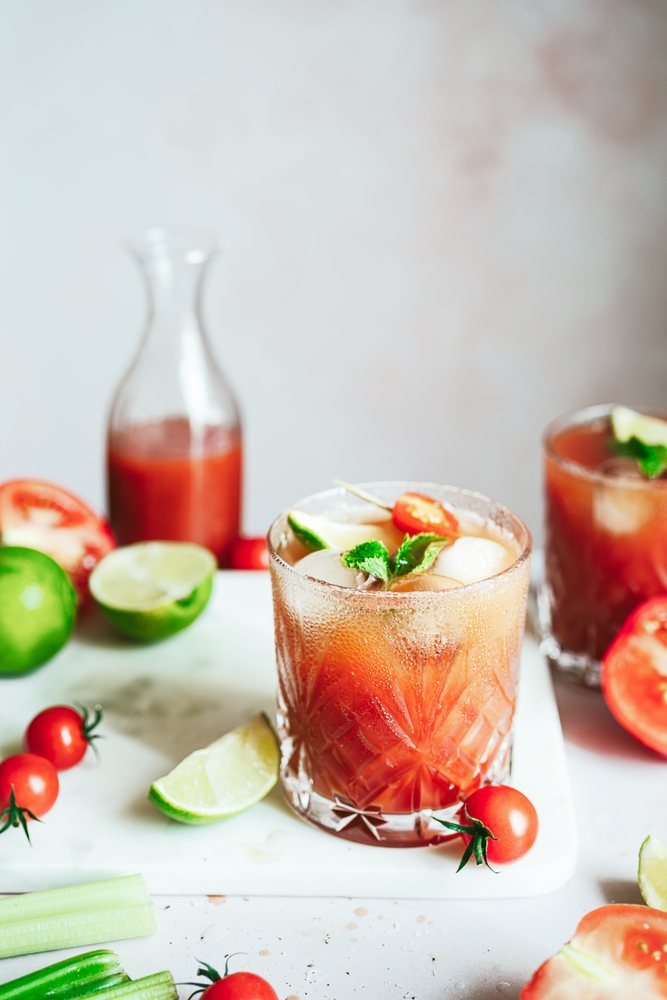 Cóctel de tomate con lima y hierbabuena en vaso tallado, con tomates cherry y lima alrededor