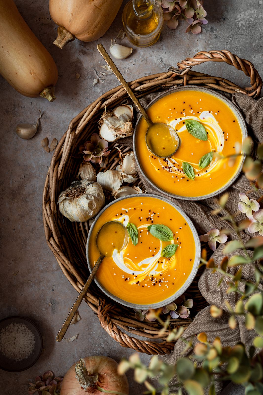 Crema de calabaza con albahaca y nata en dos cuencos dentro de una cesta de mimbre