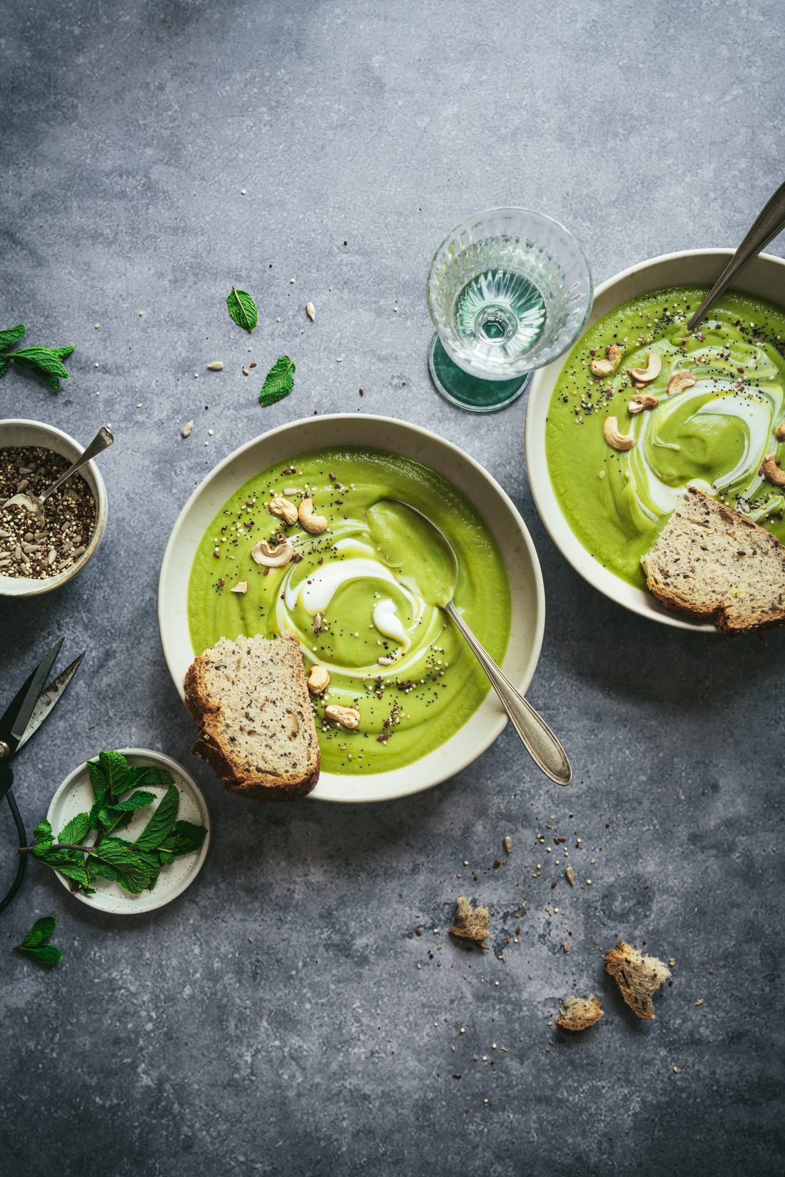 Crema verde con anacardos, semillas, menta y pan en dos cuencos sobre fondo gris