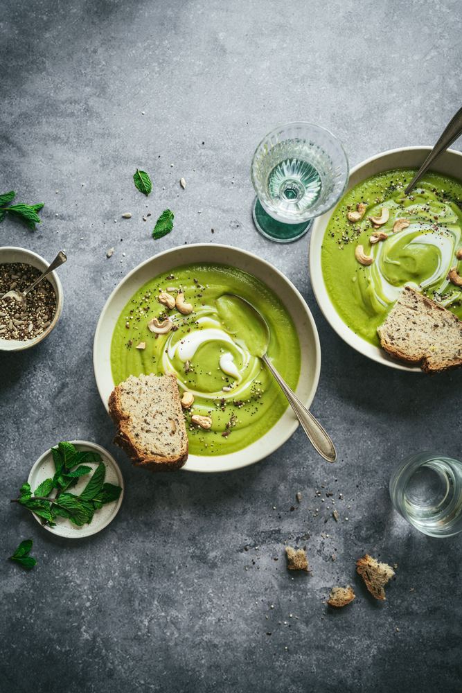 Crema verde con anacardos y pan en cuencos sobre gris