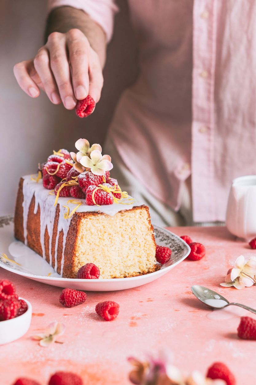 Mano decorando un cake de limón con frambuesas