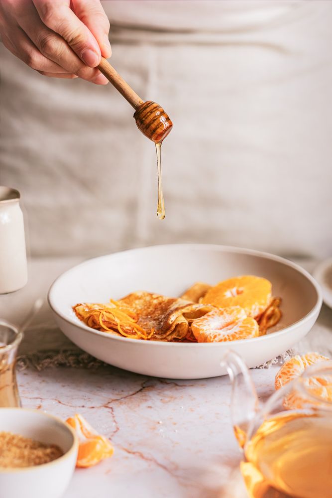 Mano dejando caer miel sobre crêpes con mandarina en un cuenco blanco
