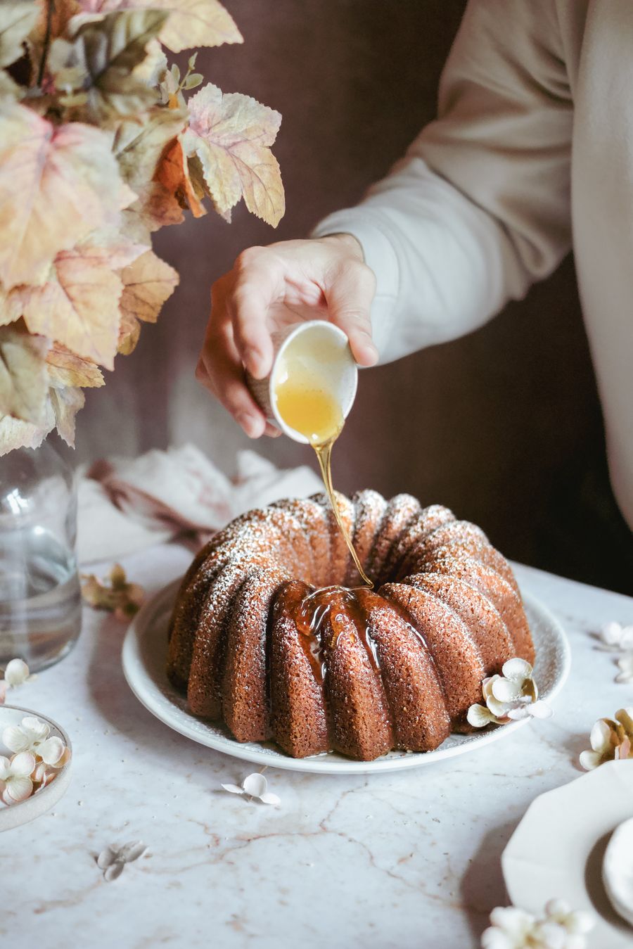 Mano vertiendo almíbar sobre un bundt cake con flores