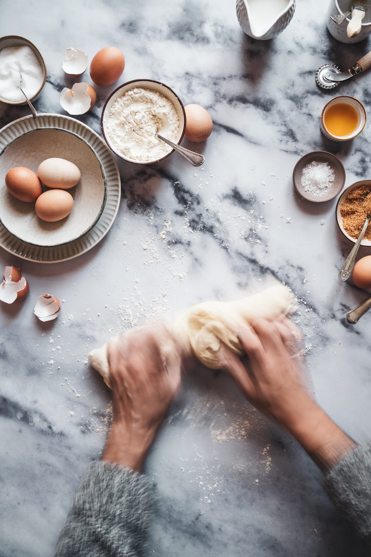 Manos amasando sobre mármol, rodeadas de huevos, harina, azúcar y leche