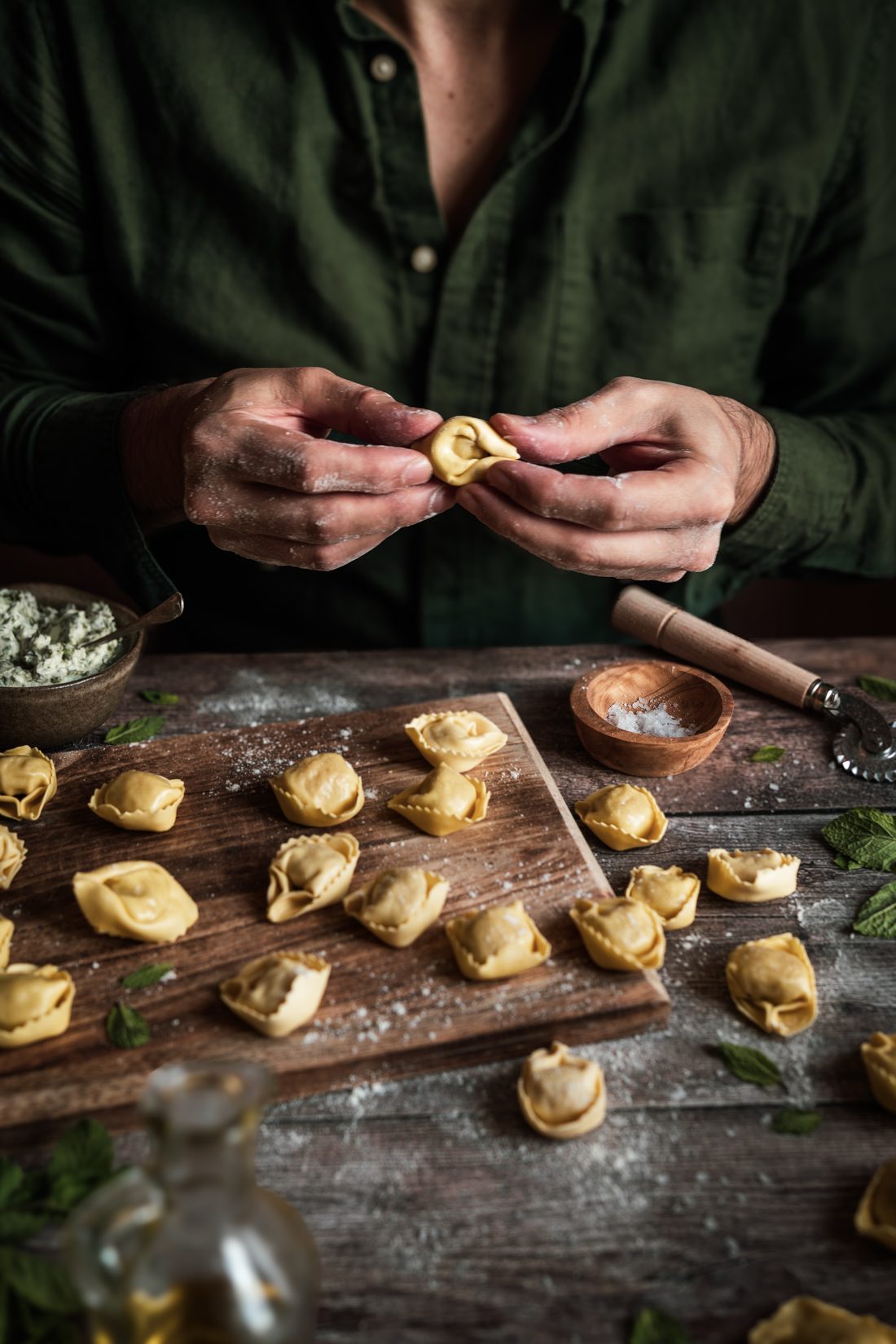 Manos formando tortellini frescos sobre una tabla de madera enharinada