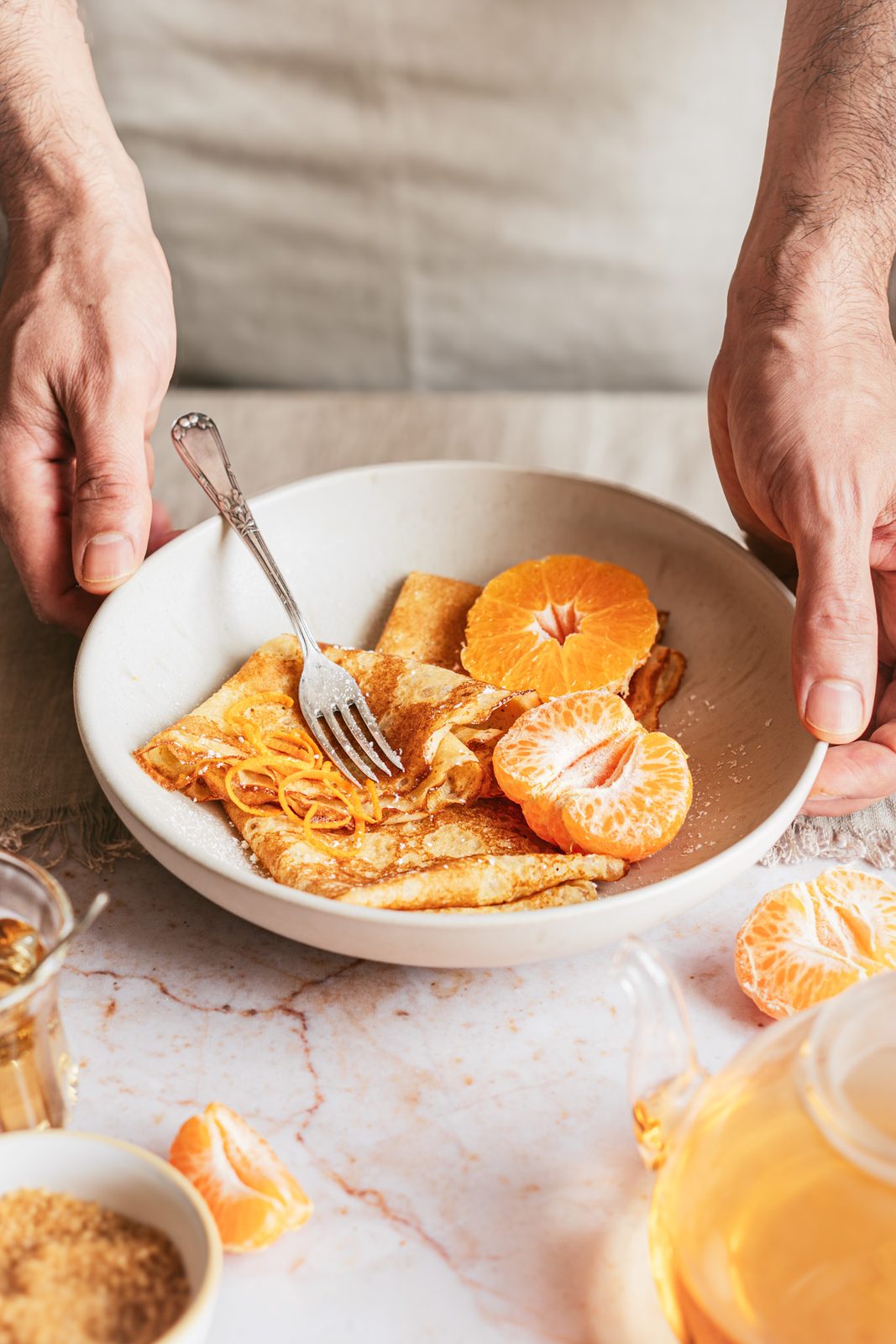 Manos sujetando un plato de crêpes con mandarina y piel de naranja