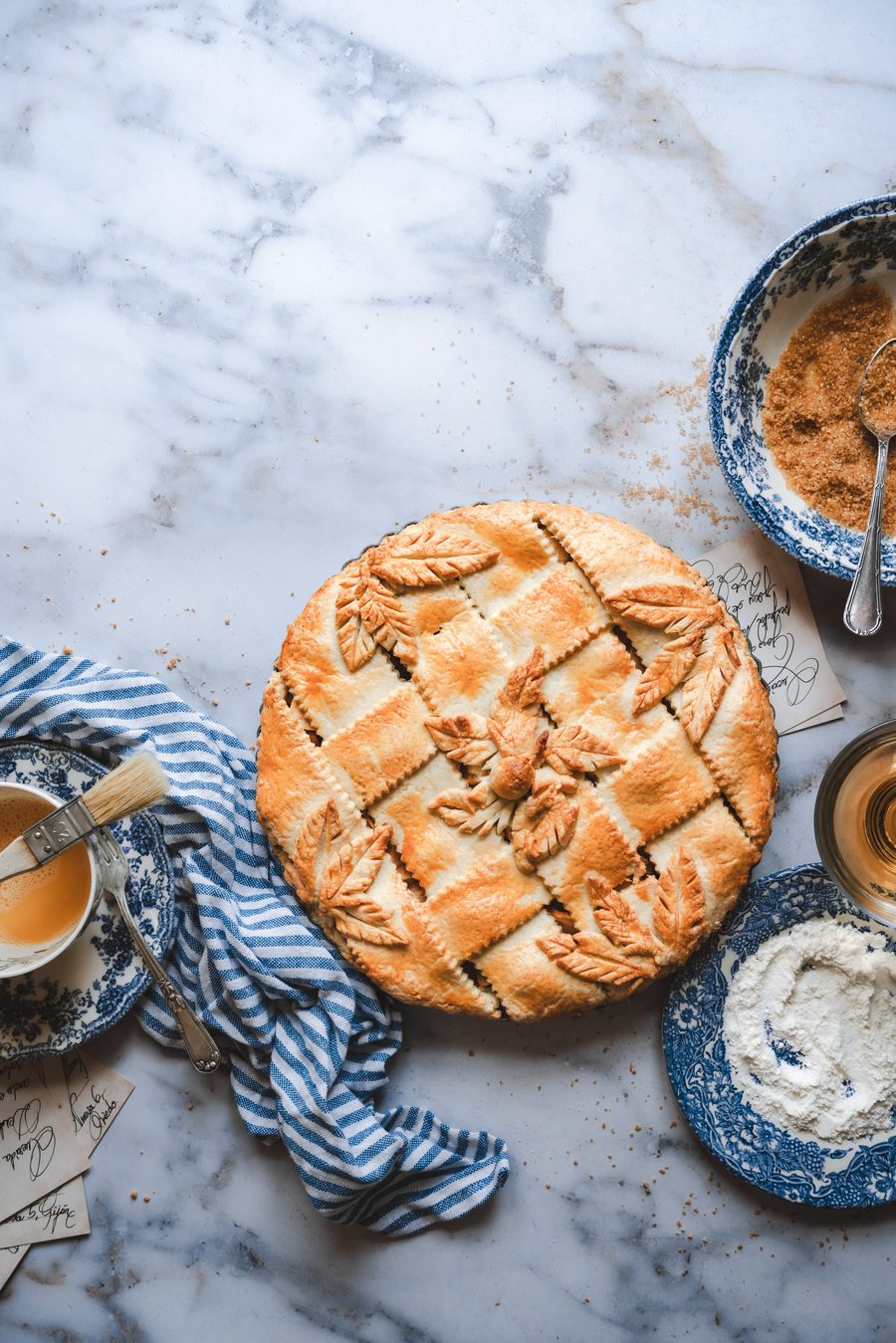 Pastel de hojaldre con hojas decorativas, loza azul y paño de rayas sobre mármol