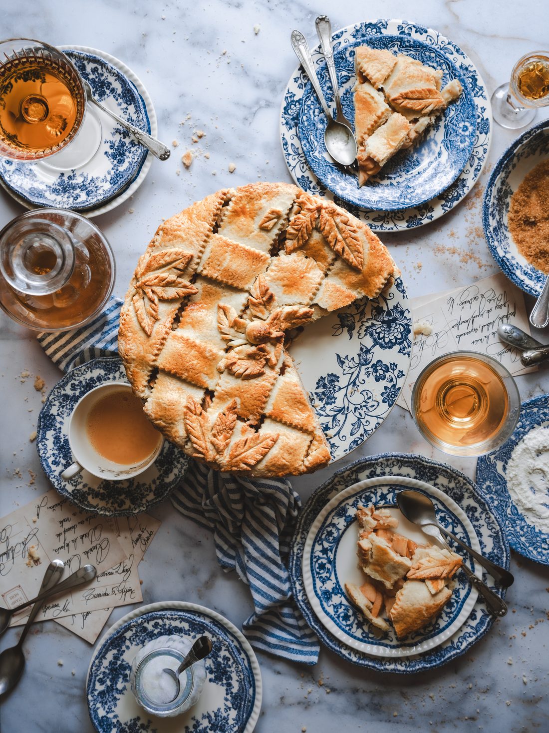 Pastel de hojaldre con hojas decorativas y porciones servidas en loza azul sobre mármol