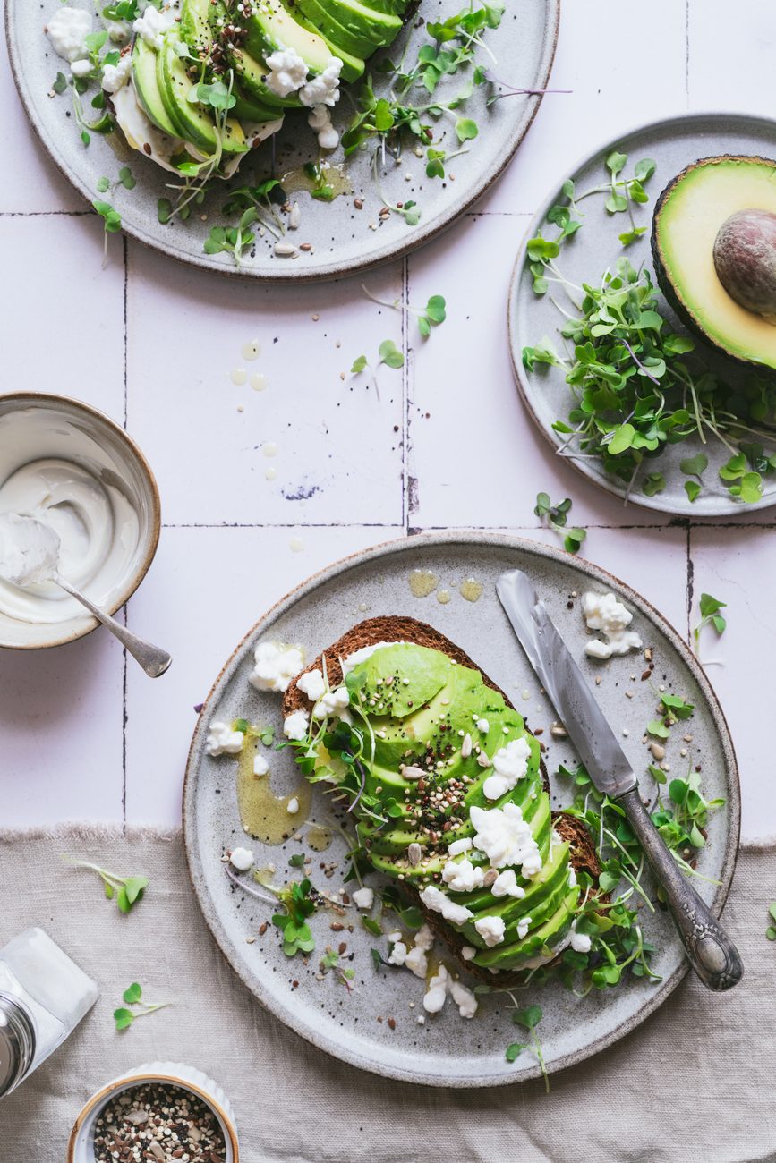Tostada de aguacate con queso fresco, brotes y semillas sobre azulejos claros