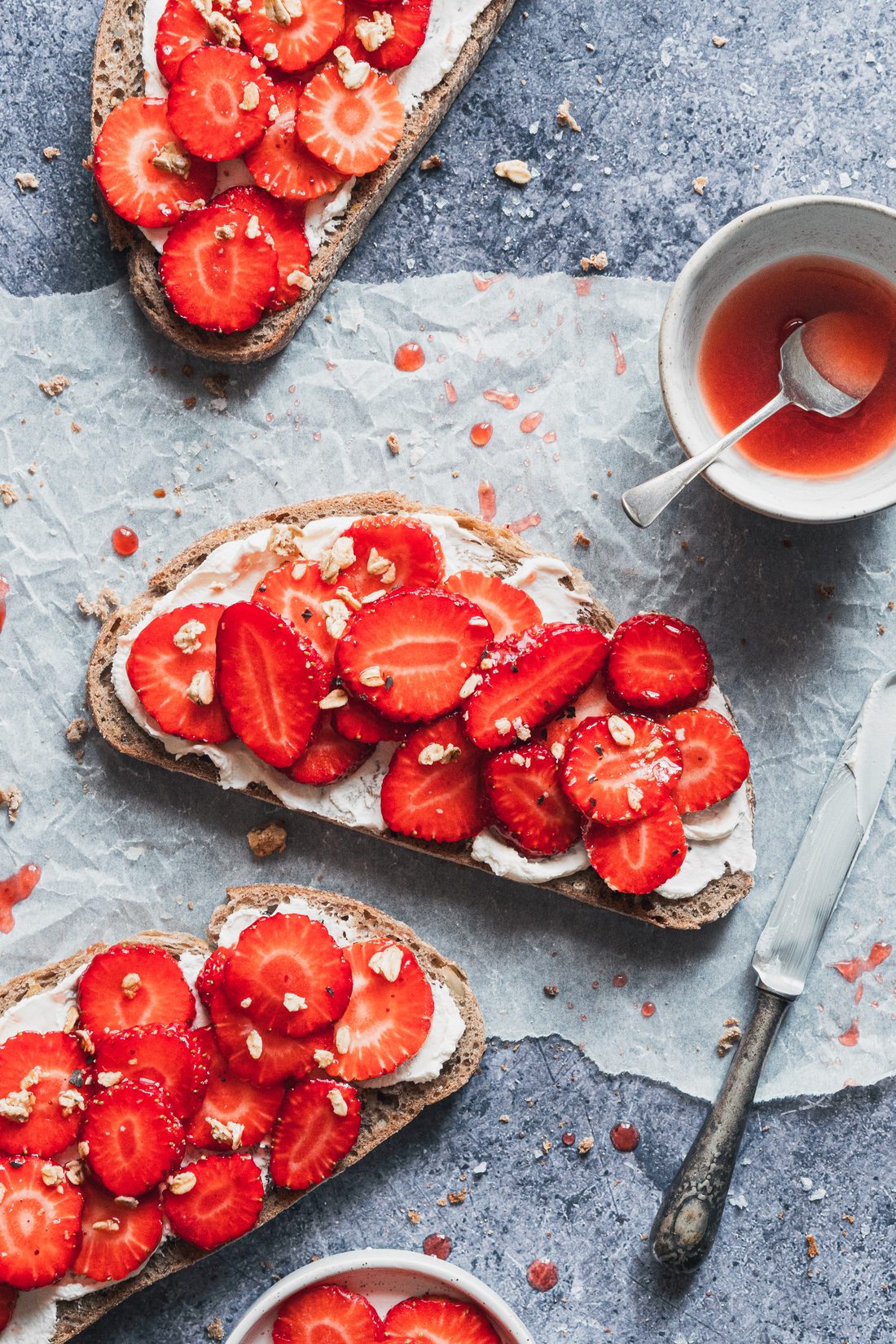 Tostadas con queso crema y fresas laminadas sobre papel de horno y fondo azul