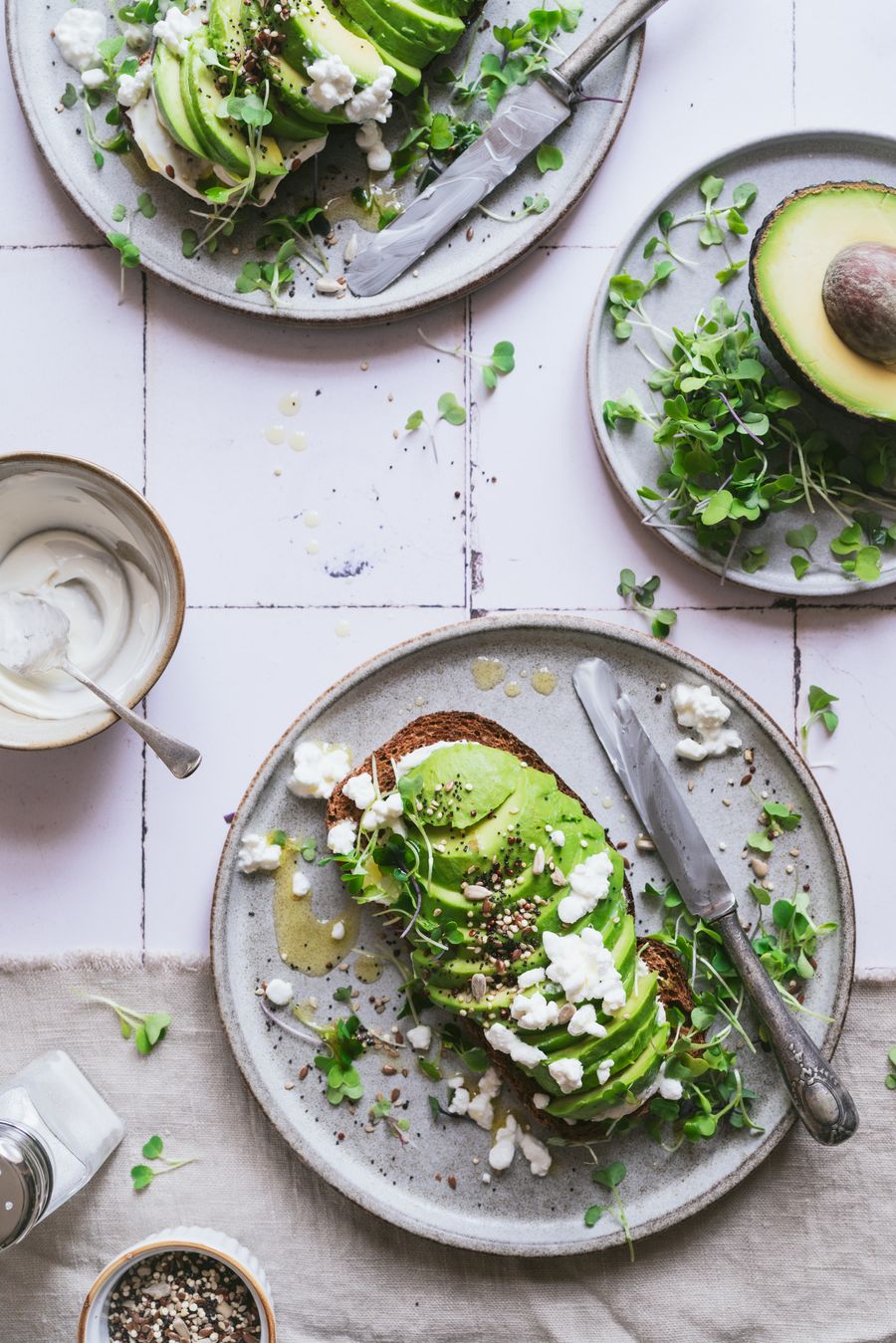 Tostadas de aguacate con queso fresco y brotes sobre azulejos claros
