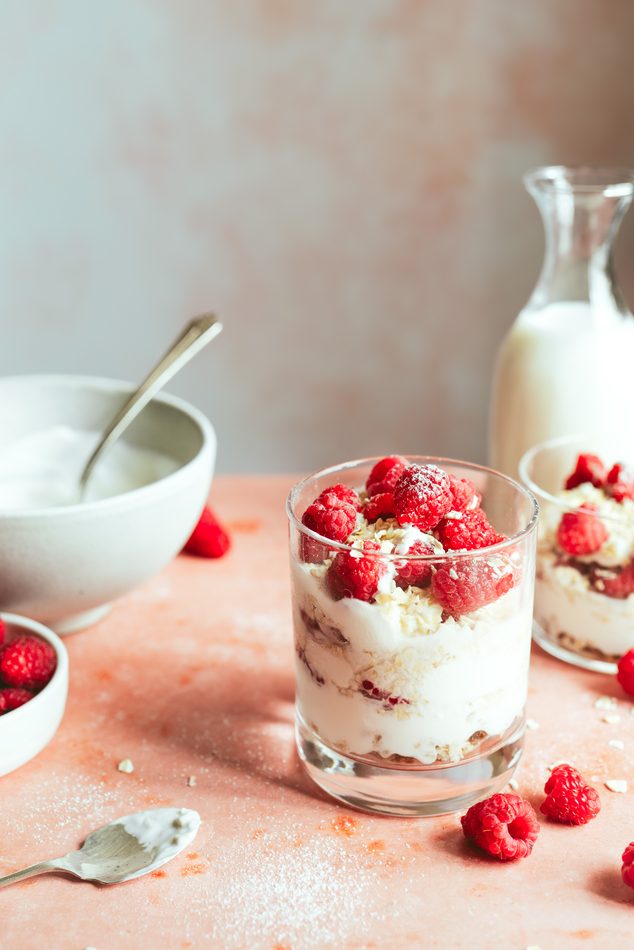 Vaso de yogur con avena y frambuesas sobre fondo rosa