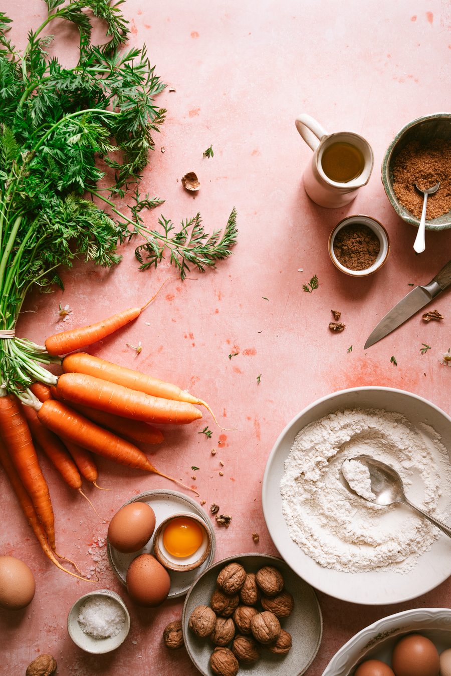 Zanahorias, harina, huevos y especias sobre fondo rosa
