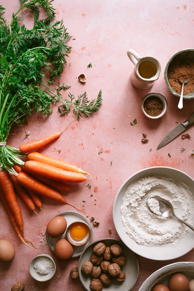 Zanahorias, harina, huevos y especias sobre fondo rosa